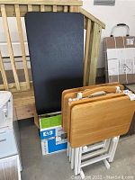 Photo showing black folding table leaning against wooden stairs with TV trays and HP printer boxes below.