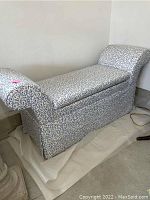 Side view of rectangular upholstered bench with curved armrests, showing fabric pattern and overall shape.