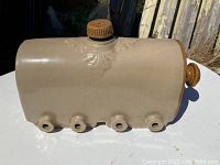 Side view of beige ceramic warming device with four spouts and a central screw-in stopper.