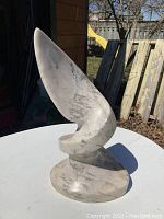 Full view of abstract stone sculpture on round table outdoors, showing overall form and base