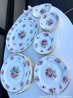 Full set displayed including plates, bowls, serving platter, and salt & pepper shakers on a round table outdoors.