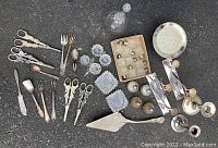 Overview of assorted silver plated serving utensils, glass salt and pepper shakers, cut glass candle holders, silver plated trays and other pieces.