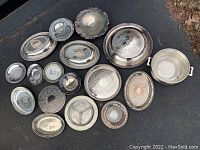 Overview of all silver plated pieces in the lot arranged on the ground showing variety of trays, bowls, and covered dish.