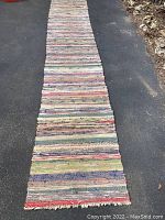 Full view of the large multi-colour rag rug laid out on pavement, showing entire length and width.