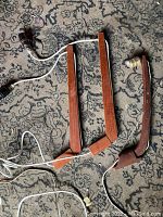 Three teak wood mid-century modern wall light fixtures with attached cords and bulb sockets laid flat on patterned carpet.