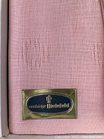 Close-up of pink linen fabric showing subtle circular woven pattern and Century Bielefeld brand label in gold and blue.