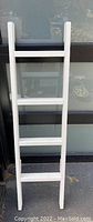 Full front view of the white decorative ladder showing four rungs and side rails.