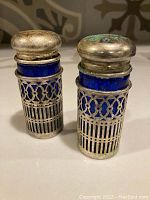 Pair of cobalt blue glass salt and pepper shakers with metal lattice holders and tarnished metal caps visible.