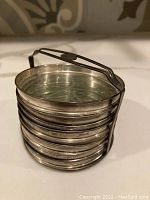 Stack of eight coasters in sterling silver holder on countertop