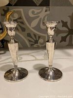 Pair of sterling silver candle holders shown side by side on a countertop with decorative backsplash visible.