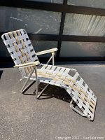 Side profile of vintage aluminum frame webbed patio lounge chair showing seat, backrest, armrests and footrest in sunlight.