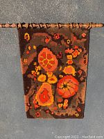 Full view of vintage hooked rug hanging on wooden rod, showing overall size and color pattern