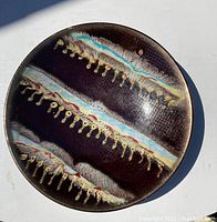Photo showing full view of round decorative ceramic bowl with dark brown base and multi-colored horizontal glaze bands with textured detailing.