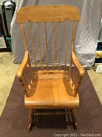 Front view of antique pine rocking chair showing hand-carved details on armrests, curved top rail, and solid wood seat.