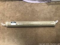 Full view of rolled green chenille fabric wrapped in plastic packaging lying on carpeted floor.