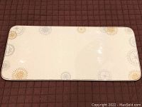 Rectangular bone china serving platter with stylized snowflake patterns in silver and gold, laid flat on a dark quilted surface.