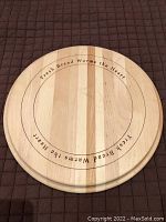 Top view of circular wooden bread board showing engraved inscription 'Fresh Bread Warms the Heart' around the recessed inner circle. Light wood with visible grain and minor knife marks.