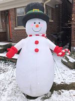 Front view of eight-foot tall inflatable snowman outdoors on snowy ground. Inflated fully, showing black top hat, red scarf, red mittens, candy cane accessory, and smiling face.