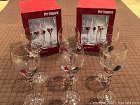 Lot includes six Pier 1 Imports wine glasses with Christmas-themed red and green glass drop stems displayed in front of two red Pier 1 Imports boxes.