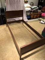 Full view of dismantled walnut single bed frame showing the headboard, footboard, and supporting side rails in a room setting.