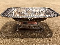 Side view of rectangular silver candy dish on pedestal with detailed filigree and cut-outs.