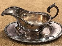 Side view of silver footed gravy boat on matching oval tray showing ornate handle and filigree border.