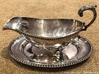Gravy boat and tray angled shot showing profile, ornate handle and beaded detail on tray edge.