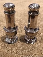 Front view of two eight-sided silver salt and pepper shakers on a carpet, showing dent on one shaker top.