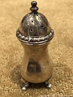 Front view of silver plated footed saltshaker showing domed perforated top and filigree band.