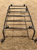 Close-up front perspective of a rectangular silver plated metal tray stand with four curved legs and ball feet, designed to support hot plates off surfaces.