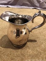 Silver plate water pitcher with ornate curved handle and wide spout featuring ice catcher, photographed from side.