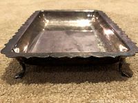 Side view of small silver tray showing scalloped edges and three visible legs out of original four, one leg broken off.