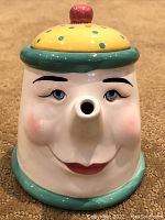 Front view of whimsical ceramic tea pot with facial features and spout as nose.