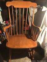 Front view of the solid wooden rocking chair showing seat, armrests, and spindle back with some surface wear.