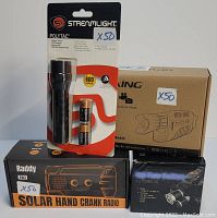 Photo showing Streamlight Polytac flashlight in packaging, Rexing night vision monocular boxed, Raddy solar hand crank radio boxed, and 3 bulb high powered headlamp boxed.
