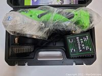 Electric ceramic tile sticking machine wrapped in plastic along with charger and adapter in black carrying case.