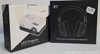Photo showing packaging boxes of LED projector and Silensys E7 headphones side by side, with model and key details visible on boxes.