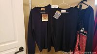 Dalkeith and Pringle sweaters hanging on hangers showing front view with tags attached.