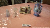 Overview of all lot items including Dresden porcelain lace figurine piano concerto, blue vase and blown glass pieces on a pink tablecloth