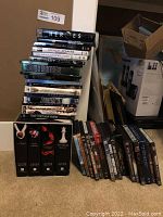 Stack of Twilight Saga hardcover books along with a large assortment of DVDs stacked on floor against wall.