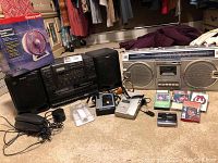 Wide view of lot showing Sony boombox, Sharp cassette recorder, two Citizen cassette players, assorted cassettes, portable battery charger, speaker and GE telephone on carpet