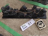 Full view of the soapstone carving showing the musher seated in the sled harnessed to four sled dogs, with accompanying MaxSold auction lot tag visible.