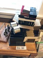 Boxed pens, pen holders, horizontal stepped file trays, and desk organizer with scissors on wooden desktop.
