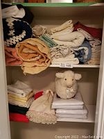 Shelves with multiple folded and rolled linens in assorted colors and a small plush sheep toy.