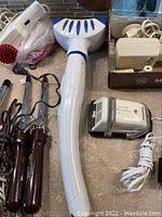 Overview of the collection including large electric massager, curling irons, and electric razor on a tiled surface.