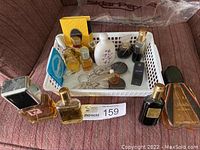 Overview of 14 small vintage perfume bottles of various shapes, materials, and colors in plastic basket and surrounding area on couch.
