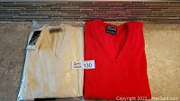 Two sweaters side by side on floor: white Dalkeith wool sweater with tags and packaging, red Chartwell acrylic sweater without tags.