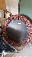 Full view of round rebounder exerciser from front, showing black jumping surface and brown leather spring guard.