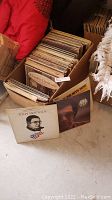 Box filled with a large quantity of vinyl records, visible album covers include Tony Mottola and others stored in a cardboard box.