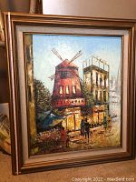 Framed Rene Caron oil painting showing a street with windmill and buildings.
